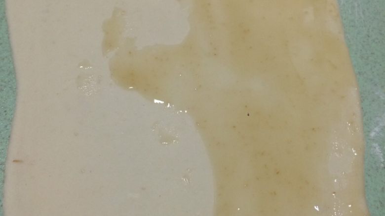 早餐美味鸡蛋灌饼,取一个剂子揉几下后擀成牛舌状,尽量擀薄一点,之后把油酥糊抹在面饼一半