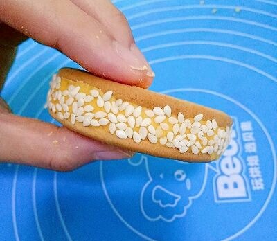 南瓜饼,取另一块饼干盖在面团上,将面团夹在中间,形成夹心,然后把饼放在芝麻里滚一圈,让饼周围都均匀的沾上芝麻
