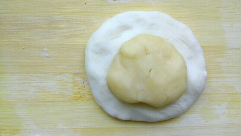 肉馅烧饼,拿一块面皮面团压平，把油酥包到里面，收口向下