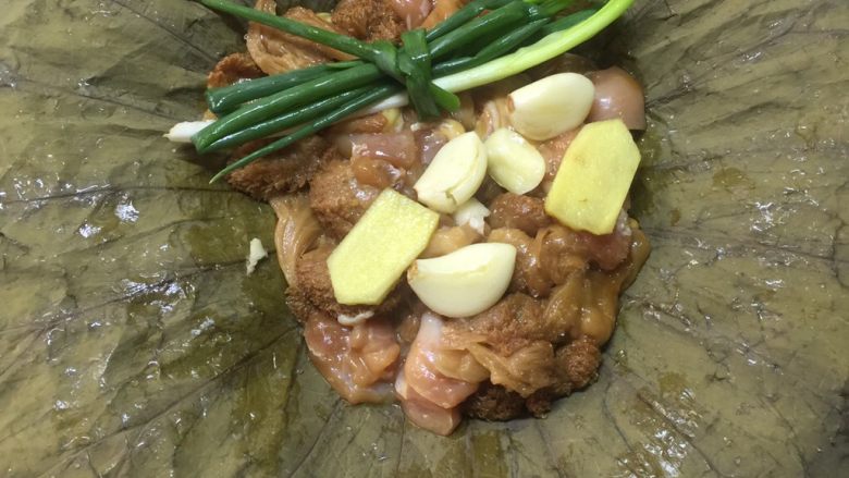荷香蒸猴头菇鸡腿肉(附如何清洗猴头菇),将荷叶铺开,放入腌制好的猴头菇鸡腿肉。表面摆上葱结,蒜子,姜。
