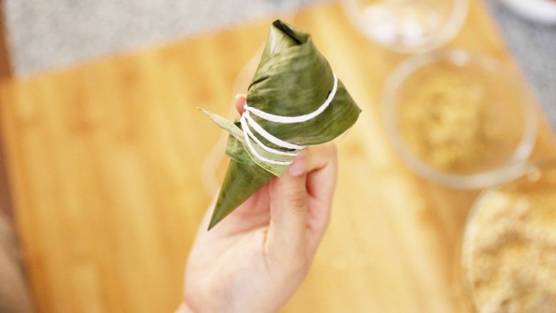 泡菜五花肉粽子,把粽叶翻下来,把粽子包裹起来,绕上棉线
