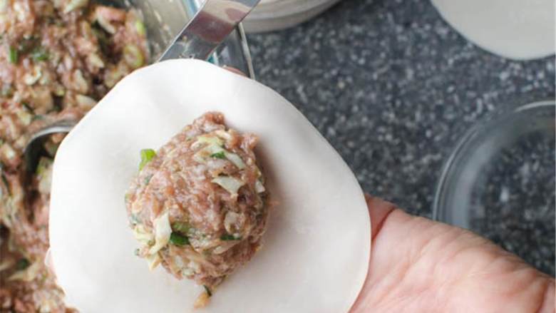 亚洲猪肉水饺,在小碗里加水放在旁边,在手上放上1片饺子皮,手指沾一点水,将水在饺皮边缘抹一圈,挖一勺馅置于饺皮中间 。