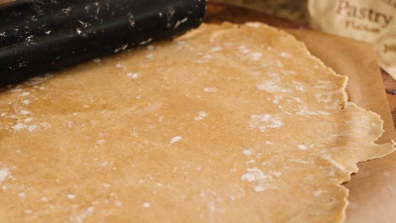 玉米番茄果挞,将生面团从冰箱取出,在上面撒上面粉,用擀面杖、酒瓶或玻璃瓶擀成0.3~0.6厘米厚的圆形面皮。