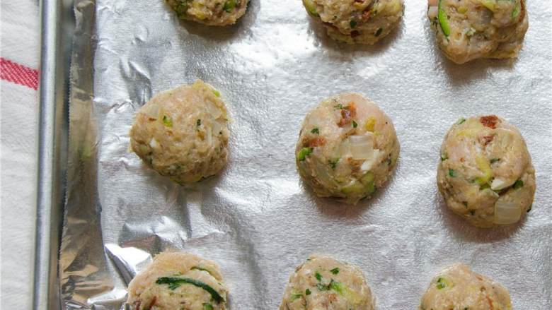 地中海风味火鸡肉丸,用一个汤勺舀取肉馅,用手揉搓做成肉丸,把它放在烤盘上,每个间隔2.5厘米左右。