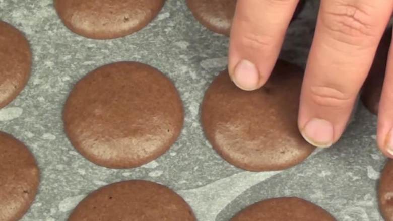 Nutella巧克力马卡龙,把面糊倒入裱花袋里,在烤纸上挤上一团团圆形,压成平滑表面,放置1小时。一旦表面不粘的话,就能放入烤箱里了。将烤箱预热到150度。