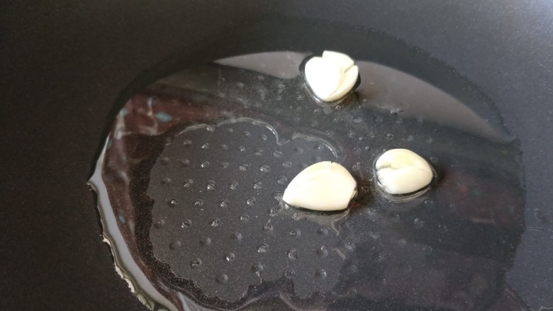 快手下饭菜:青椒肉丝,蒜用刀背压一下,锅中倒入食用油,烧热后放入蒜瓣炒香。