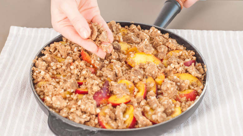 桃子派,制作顶部装饰配料:混合剩余的焦黄油、黑砂糖、面粉、杏仁、甜胡椒粉和盐。用手将其搅拌成一大块。捏碎撒到桃子上。以175℃烤40分钟,或直至派变成金棕色,且用牙签插入后抽出,仅粘上些许湿润颗粒。放凉15分钟后即可享用。