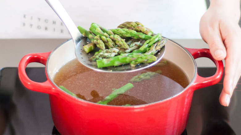 意大利熏火腿豌豆芦笋炖饭,将高汤煮沸,然后放入芦笋茎,煮2-3分钟。捞出芦笋,过一遍冷水。滤干后,放到铺好厨房纸的盘子上。芦笋尖也重复此操作。
