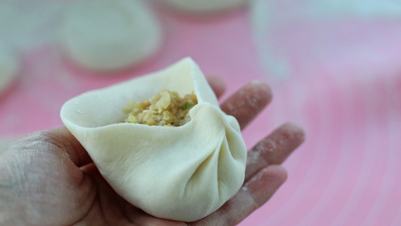 东北猪肉酸菜馅包子,左手托住底部,用右手的拇指和食指沿着边缘一圈捏出褶状