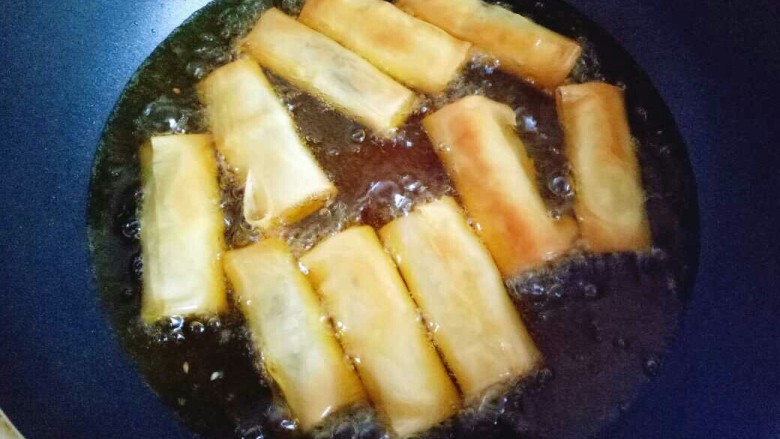 炸春卷,转中火,底部金黄时,用筷子翻一面,两面金黄即可捞出。