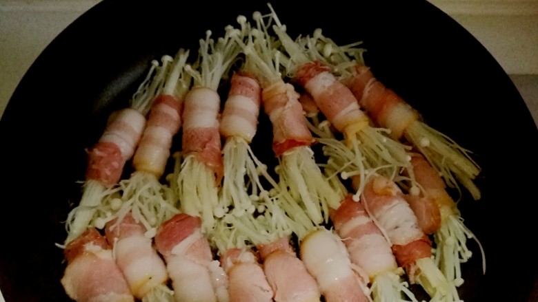 培根金针菇卷,再把卷好的金针菇一个个地摆放到平底锅里，小火煎
