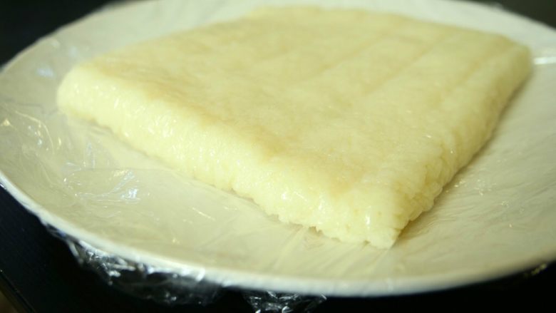 红糖糍粑,蒸熟后糯米饭取出碾碎。我是把饭放在袋子里用手揉碎的,中间也用了擀面杖帮忙。不用弄太碎,毕竟糍粑就是要有碎米粒的口感呀。然后把碾碎的米饭平铺在模具里,我用的是饭盒。底下铺了保鲜膜方便取出。上面也用了保鲜膜保湿。