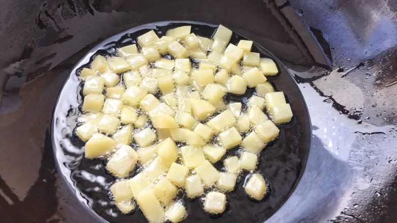 土豆腊肉焖饭,土豆切好后防止氧化，马上放锅里用油炸干，当然啦！炸土豆丁目的是为了等一下焖煮时不会煮散烂，炸过的土豆口感更佳。