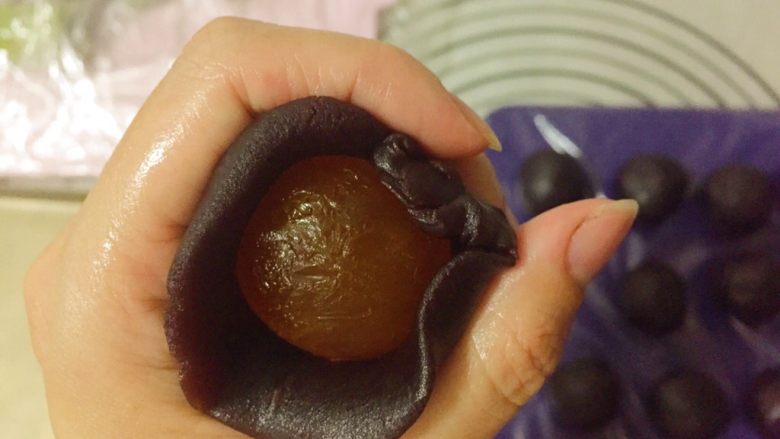 蛋黄千层酥,取一个豆沙馅按扁包入一个蛋黄,用手搓圆。
