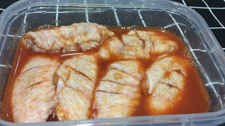 奥尔良煎鸡翅,鸡翅放入保鲜盒中,倒入烤肉料,再加入少许橄榄油,戴上手套多抓几下。然后盖上保鲜盒腌制一夜