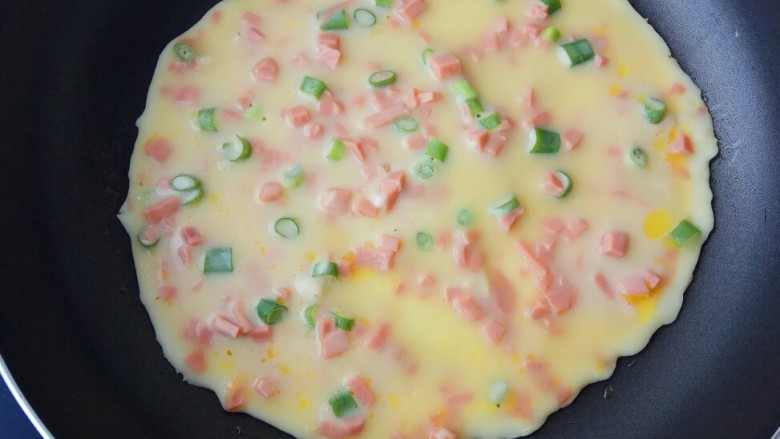 快手早餐~火腿葱花饼,取平底不粘锅,刷少量油,舀入两勺面糊,摊成圆饼