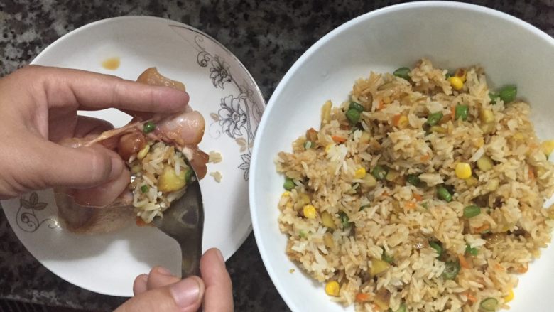 鸡翅包饭,一只手拿着去骨腌制好的鸡翅,另外一只手用勺子将炒好的饭塞进鸡翅里面,塞满就可以,不可以过涨,这样烤的时候,鸡翅会裂开的。