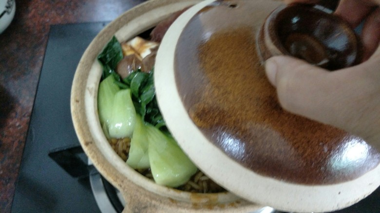 腊肠煲仔饭,把青菜放上去,盖上砂锅盖小火煮大概1分钟后熄火