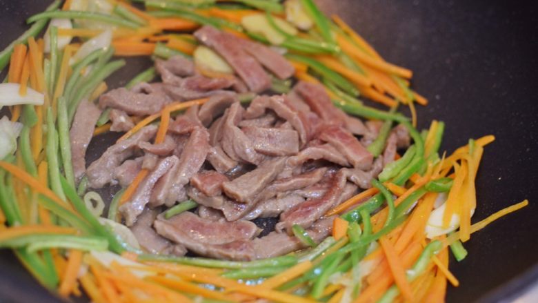 牛肉炒乌冬面,把青椒和胡萝卜拨到锅边,牛肉放中间,炒到还没有完全变色。