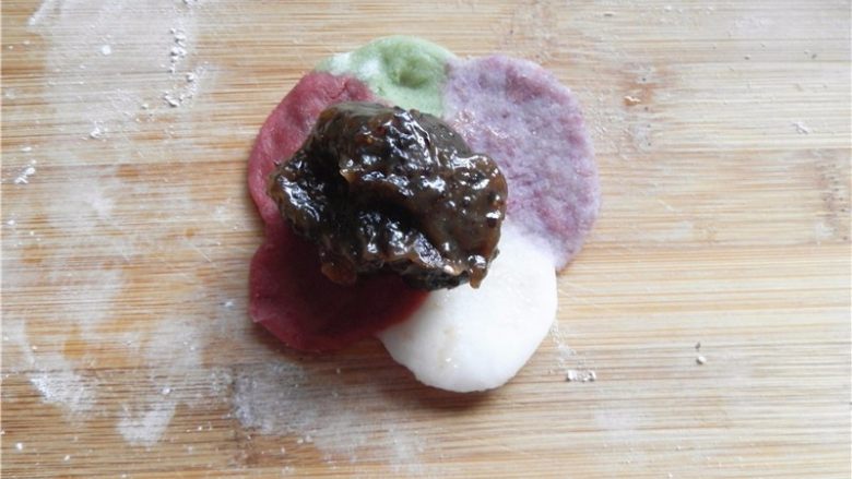天然彩色冰皮月饼,用擀面杖将饼皮擀成中间厚、周围薄,将25克枣泥馅放饼皮中间(桌面撒少粉熟糯米粉)。
