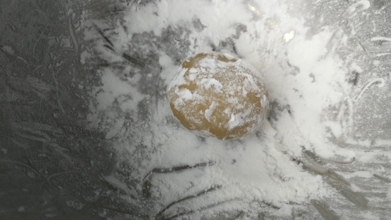 广式莲蓉蛋黄月饼,盆子里倒入玉米淀粉做手粉防粘,包好的月饼团成椭圆形放入玉米淀粉里滚一圈,轻轻拍去多余的粉