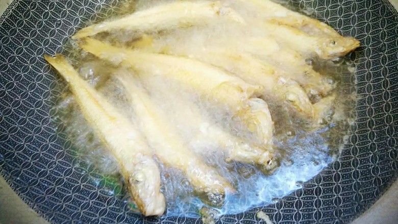 油炸沙尖鱼,将鱼一个一个放入锅,要隔间隙,用筷子不停翻动防止黏连,以文火炸至表面金黄即可。