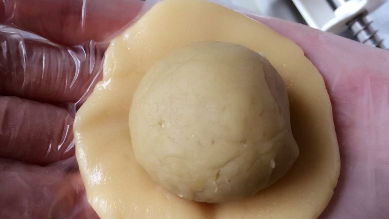 广式栗子蓉月饼,把饼皮按成圆饼,放上馅料包好。