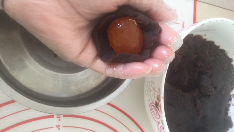豆沙麻薯蛋黄酥,把豆沙按扁放入蛋黄,用虎口网上推,大概就是左手按着蛋黄,右手虎口转着往上推,豆沙有油所以有点裂了稍微整下捏下就好了