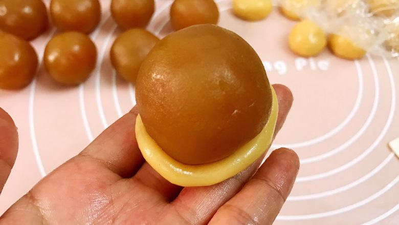 广式低糖莲蓉蛋黄月饼,取一份饼皮稍稍压扁,一手托住饼底,一手用虎口慢慢往上推(很多朋友不会推皮,就把饼皮擀成很大一块去包,我不建议这样做因为会有空气进入,导致烤好的月饼鼓包不好看)