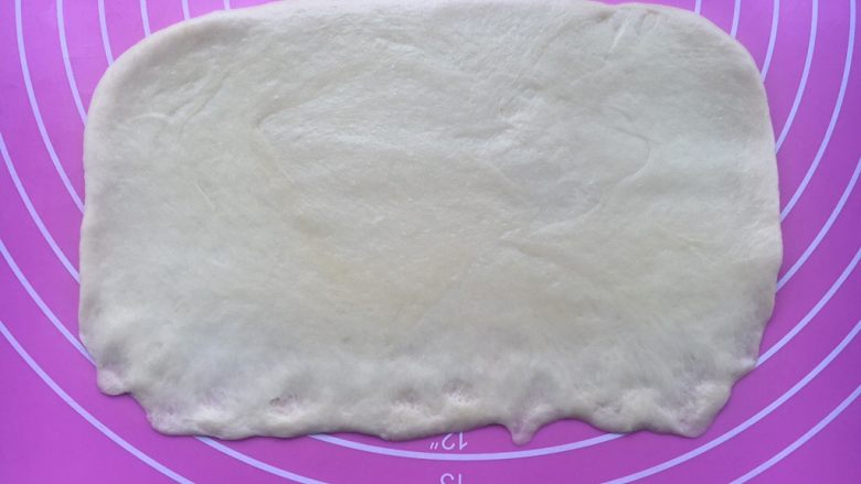 中种炼乳排包,取一个面团擀开成长方形,靠近身体这边的面皮碾薄一些,便于收口