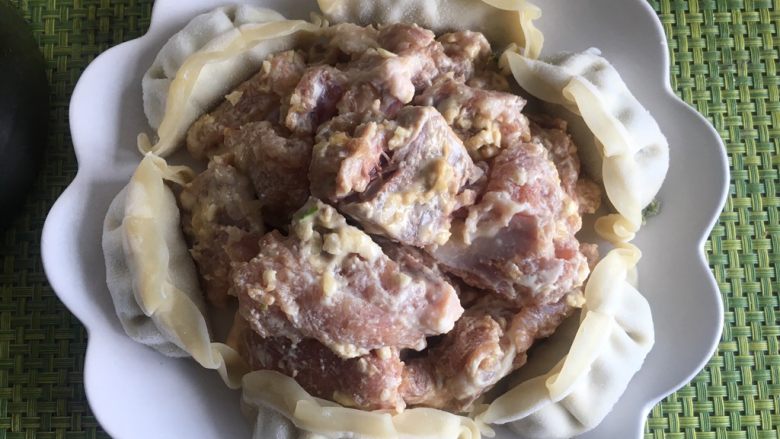 排骨蒸饺,盘子的中央堆放腌制好的排骨,四周围绕一圈饺子