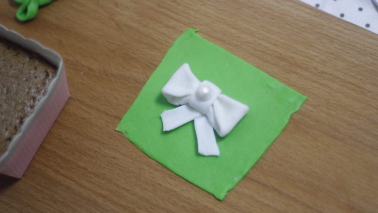 零基础纸杯翻糖蛋糕,带子沾点水贴在蝴蝶结底部,“结”上面再加一个大号的装饰珍珠糖。