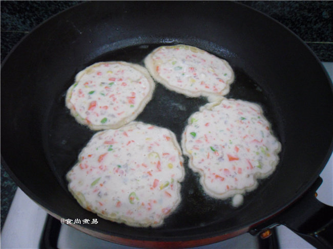 虾仁煎饼,用汤勺舀起面糊,均匀摊在煎锅上面,一勺糊就摊成一个饼,煎至底部凝固