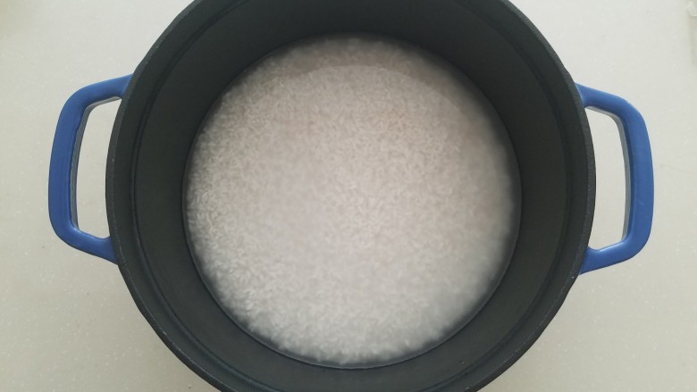 广式腊味煲仔饭,用油刷把珐琅锅底和锅壁刷一层薄油,将泡好的米连同泡米水一同倒入锅中,轻摇锅体使大米均匀铺满锅底。