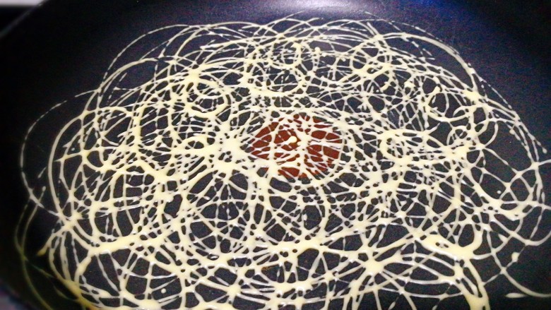 鸡蛋金丝卷,平底不粘锅开小火,画小圈挤出面糊。 开中小火,我在不粘锅中没刷油,也没有粘锅,你怕粘锅,可以在锅中加入一滴油抹匀。 画圈圈挤出面糊,形成镂空图案,煎至表面凝固。