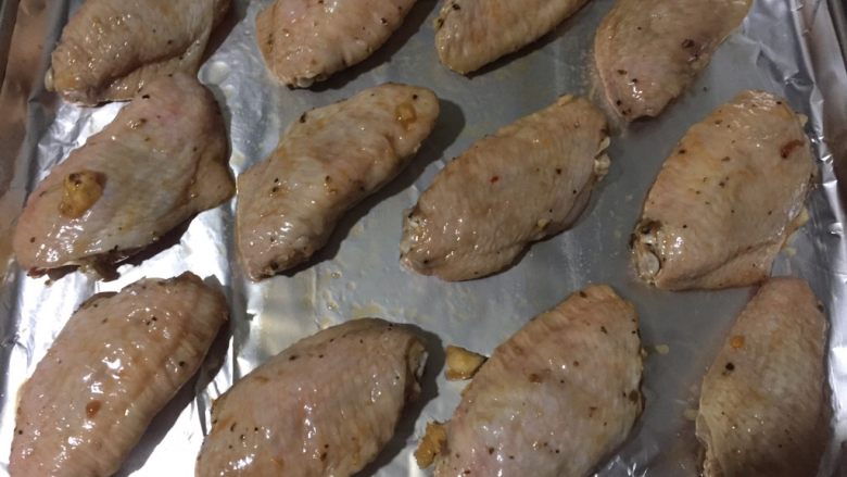 蜜汁烤翅,烤箱预热至180度,在烤盘上铺上锡纸,锡纸表面刷一层油,将鸡翅稍甩干调料后正面朝上放在锡纸上,鸡翅表面刷一层油,放入烤箱,烤12分钟