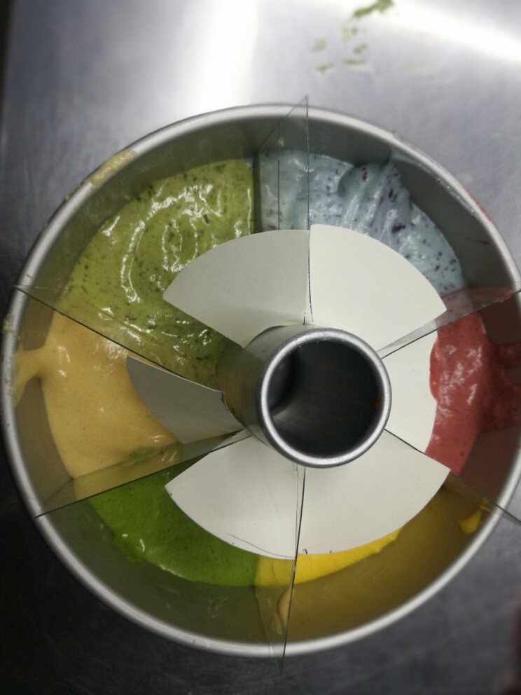 一次性做出六种口味的戚风蛋糕,把6个颜色拌好的面糊装入6个裱花袋中,挤在模具中。挤的时候要6个颜色同时挤,先挤到模具的一半,这样面糊不会流到另个颜色中,再挤剩下的面糊。然后轻轻的垂直提起当中的隔片。震一下模具排出面糊中的空气。烤箱提前预热