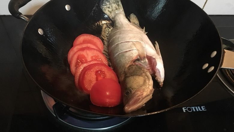 鲜掉眉毛的奶汤鳜鱼,等到晃动锅子能感受到鳜鱼自由滑动时,把它拨在一边,下番茄略炒。