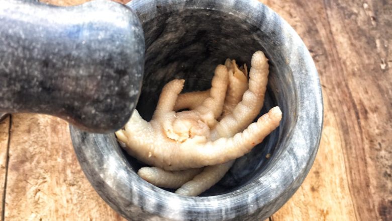柠檬舂鸡脚,传统做柠檬舂鸡脚,把蒜瓣放入臼里,(一般使用的都是木臼有脸盆那么大,舂深有几十厘米高)放入几颗小米辣舂碎。然后放入豇豆舂碎,洋葱舂碎,最后放入鸡脚舂碎,不用太烂。再用挤压器挤出柠檬汁,挤到臼里,挤过的柠檬同样放入臼中。放入各种调料,盐,味精,柠檬汁,辣椒酱,芫荽(当地有两种,大小芫荽),胡萝卜丝,花生碎等调料。因为自己用的是小舂条件上有所限制,把舂好的调料舀放大盘中,再把冰镇的鸡脚放入舂中舂碎。