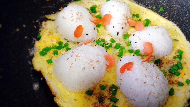 剩米饭百种做法+小老鼠抱蛋煎饭团,和白芝麻,盖锅盖。1分钟后,开盖,晃动一下锅,抱蛋饭团能移动,蛋饼边缘金黄,出锅。用剪成长短小段的<a style='color:red;display:inline-block;' href='/shicai/ 523'>粉丝</a>装上胡须和尾巴。Q萌香酥的抱蛋饭团就做好了。
