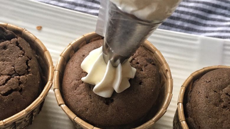 家有烤箱+快手的巧克力杯子蛋糕,将奶油放入裱花袋,涂在蛋糕上,用抹刀抹平