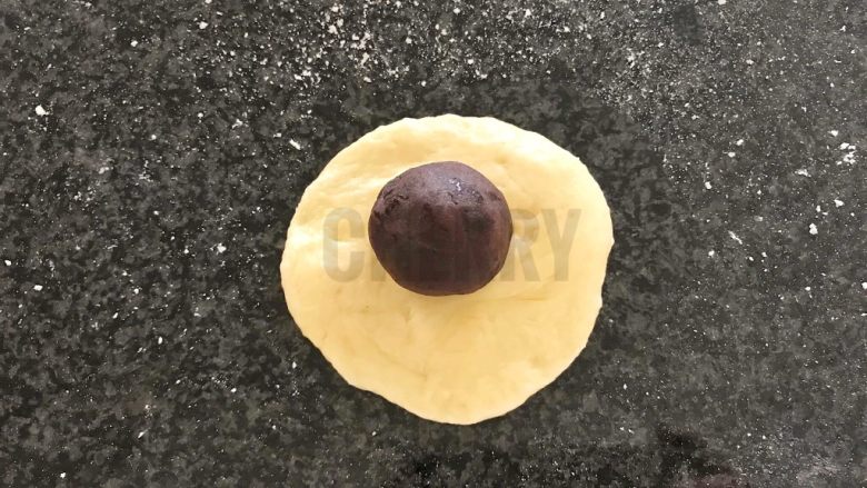 #家有烤箱#黑芝麻豆沙面包,将醒发好的面团,用擀面杖擀成圆形,上面加一颗豆沙丸子,