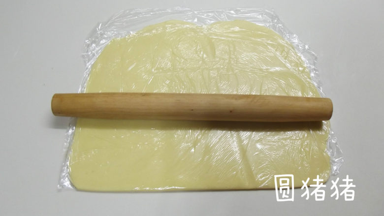 南瓜鬼脸夹心饼干,取一张大的保鲜膜,将面团放入其中,再在表面覆盖一张大的保鲜膜。用擀面棍将面团擀成3mm厚的长方形。