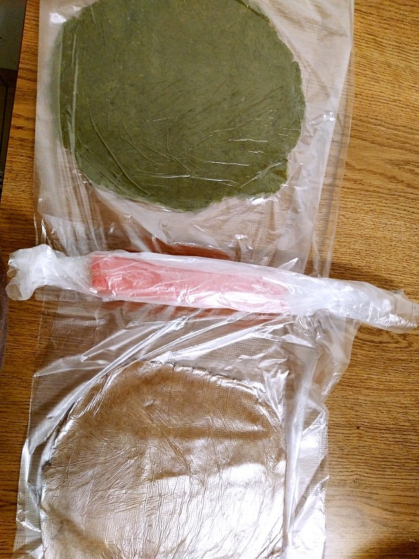 红芯猕猴桃饼干,打发好的黄油团平均分成三份，170克面粉也分成三份分别加入，再依次加入红曲粉抹茶粉可可粉，面团不要揉太久以免口感不好吃。把红色面团揉成长条冷冻10分钟，绿色棕色面团擀成和红色面团一样长度，也冷冻10分钟。