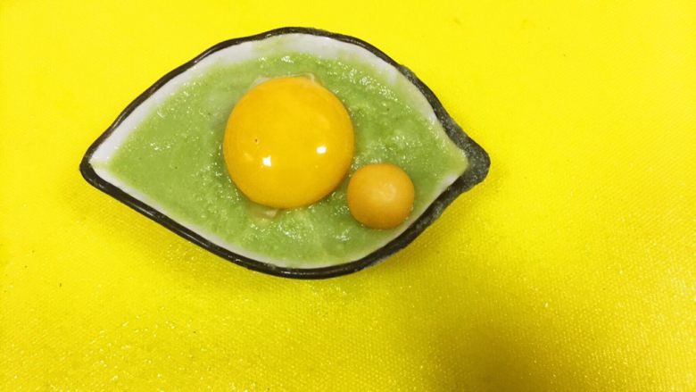 宝宝造型辅食之@@童真的眼睛(藜麦米粉,蛋黄加多种蔬果),这部需要一个这样树叶形状的小碟子,像眼睛一样,其实是个味增碟。然后把鸡蛋黄放在中间,一颗菇娘做它的反射点,像卡通人物的眼睛画的时候都是有这个泪珠的,显得水灵立体,这步,菇娘可以先不放,因为蒸熟会变色。哈哈,然后我们同样拿去蒸熟,大概大火3分钟就可以了。