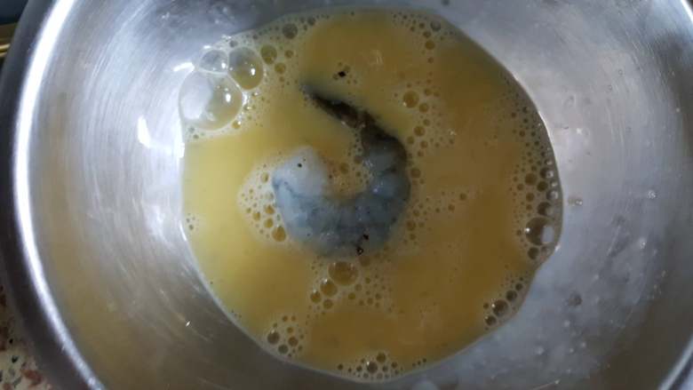 黄金凤尾虾,10.取一个腌制好的虾仁放在鸡蛋液中,使其沾满蛋液。