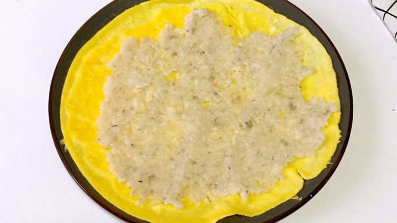 宝宝辅食之虾仁莲藕蛋卷,蛋饼上均匀铺上虾泥馅料,用勺子压紧压实。