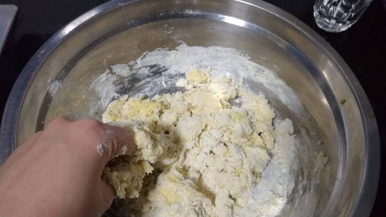 面包入门基本功之黄油面包卷,蛋液倒入面盆,用手指捏至没有明显干粉。期间可以视情添加调整用的20克水。