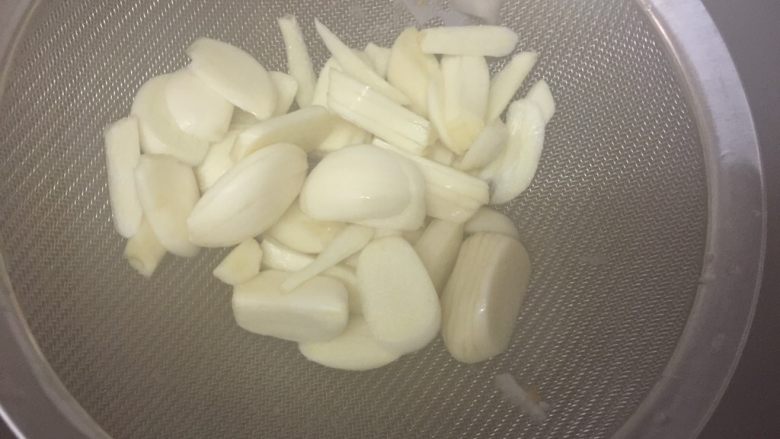 滋味泡藕,蒜头片用筛子装着,放入正在烧开的水里焯5秒即可