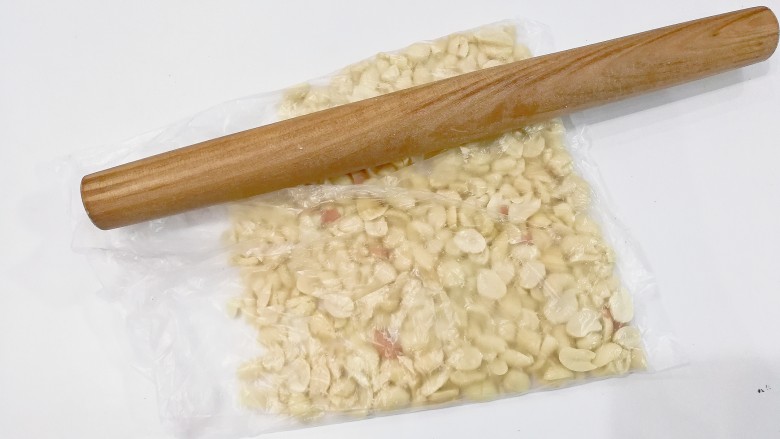蔓越莓花生牛轧糖,取100克花生仁放入保鲜袋用擀面杖稍微压碎一点;(也可以放整颗的,依个人喜好吧)
